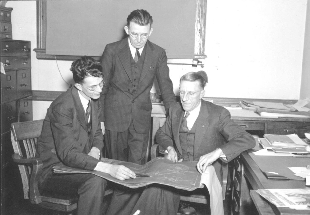 Marston, Tague, and Markuson working around a blueprint